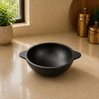 Black cast iron bowl on a beige countertop with decorative items in the background