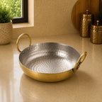 Hammered metal pan with gold handles on a beige surface
