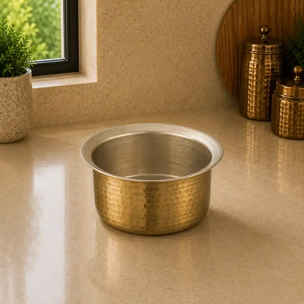 Gold metallic bowl on a beige surface with decorative jars and a plant in the background.