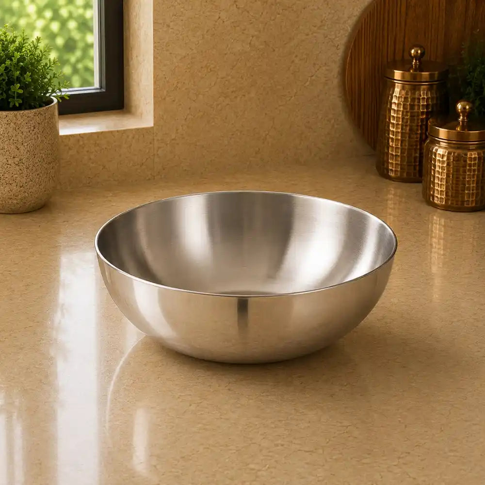 Stainless steel bowl on a beige countertop with decorative jars and a plant in the background.