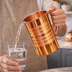 Polished copper water jug with lid and handle placed on marble kitchen countertop