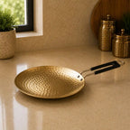 Gold frying pan with black handle on a beige countertop