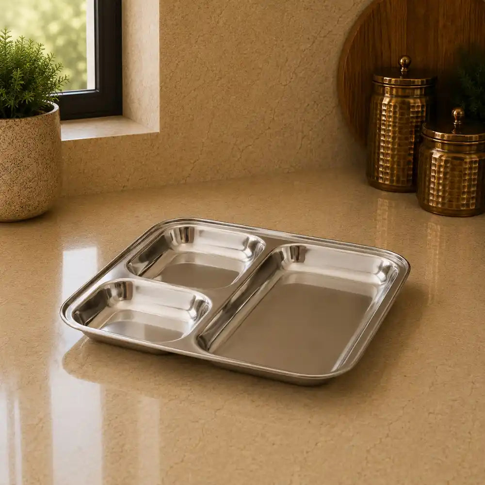 Stainless steel divided tray on a beige countertop with decorative jars and a plant in the background.