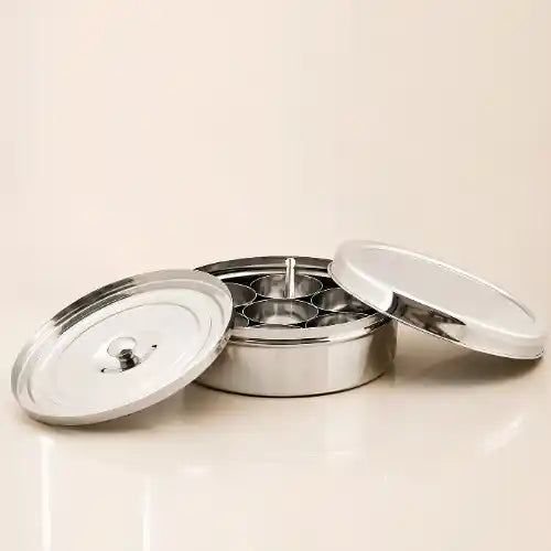 A stainless steel multi-compartment food container with its two lids off, displayed on a light beige background.