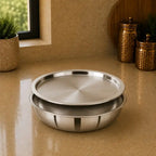 Two stainless steel trays on a beige surface with decorative jars and plants in the background.