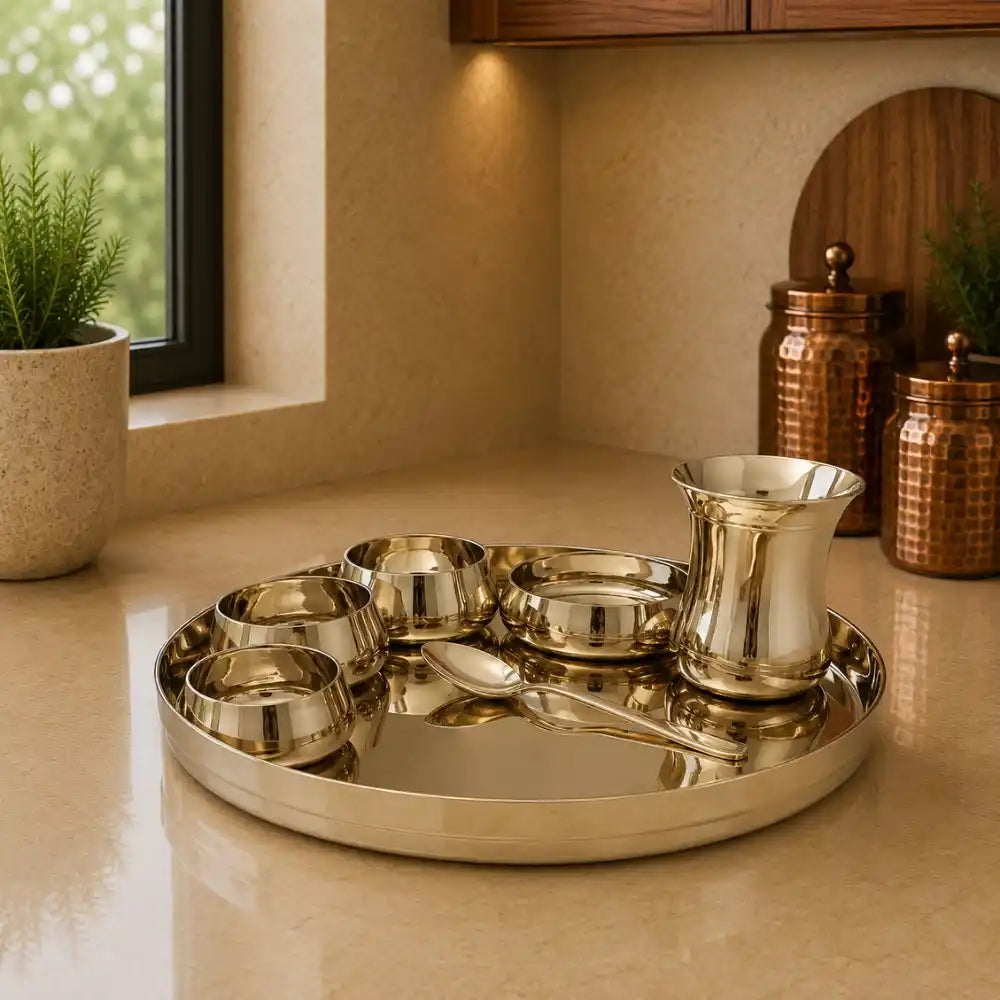 Set of silver platters, bowls, and a pitcher on a beige surface with a window and plants in the background.