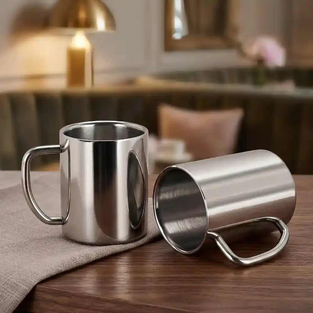 Two stainless steel mugs on a wooden table with a blurred indoor background