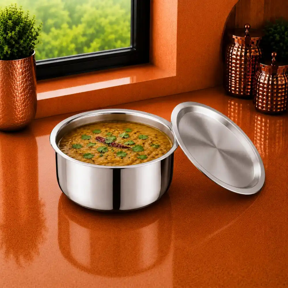 Triply stainless steel container with matching lid placed on a modern orange kitchen countertop near a window. Premium food-grade mirror-finish storage container designed for storing cooked food, rice, dal, curries, vegetables, and everyday kitchen essentials. Durable, rust-resistant, hygienic, and suitable for daily household use.