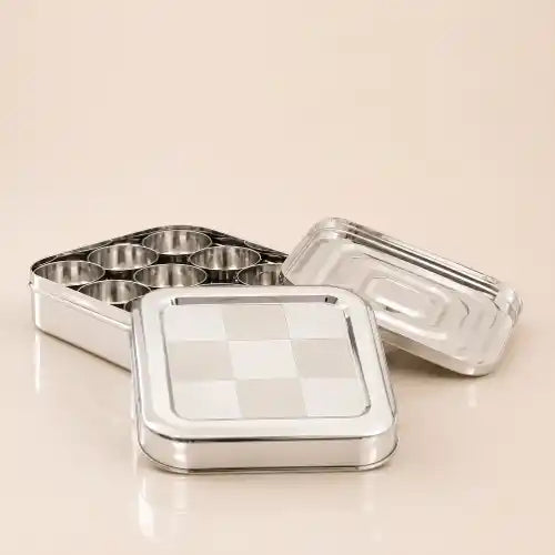 A stainless steel square lunch box with a checkered lid, shown open with its tray and separate lid on a light beige background.