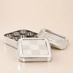 A stainless steel square lunch box with a checkered lid, shown open with its tray and separate lid on a light beige background.