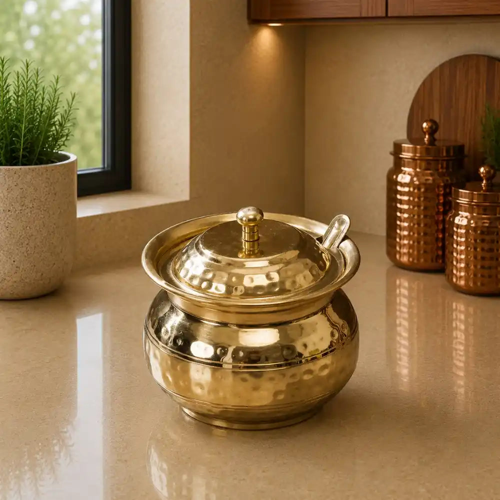Gold metallic pot on a reflective surface with decorative jars and plants in the background.