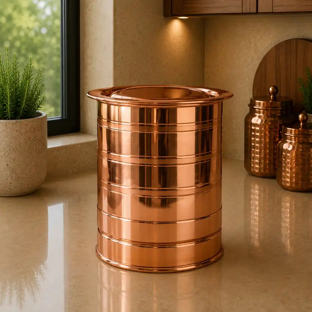 Copper trash can on a countertop with decorative jars and a plant in the background.