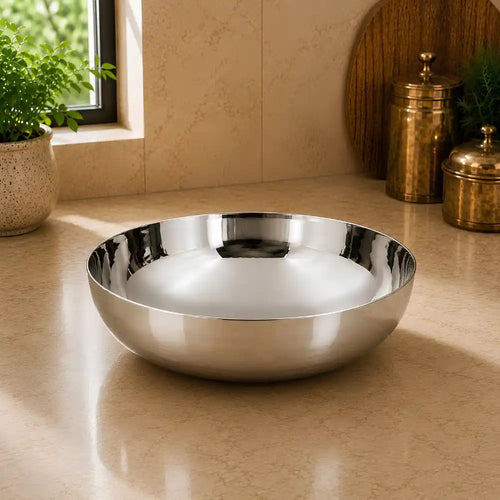 Silver bowl on a beige countertop with decorative items and a plant in the background.