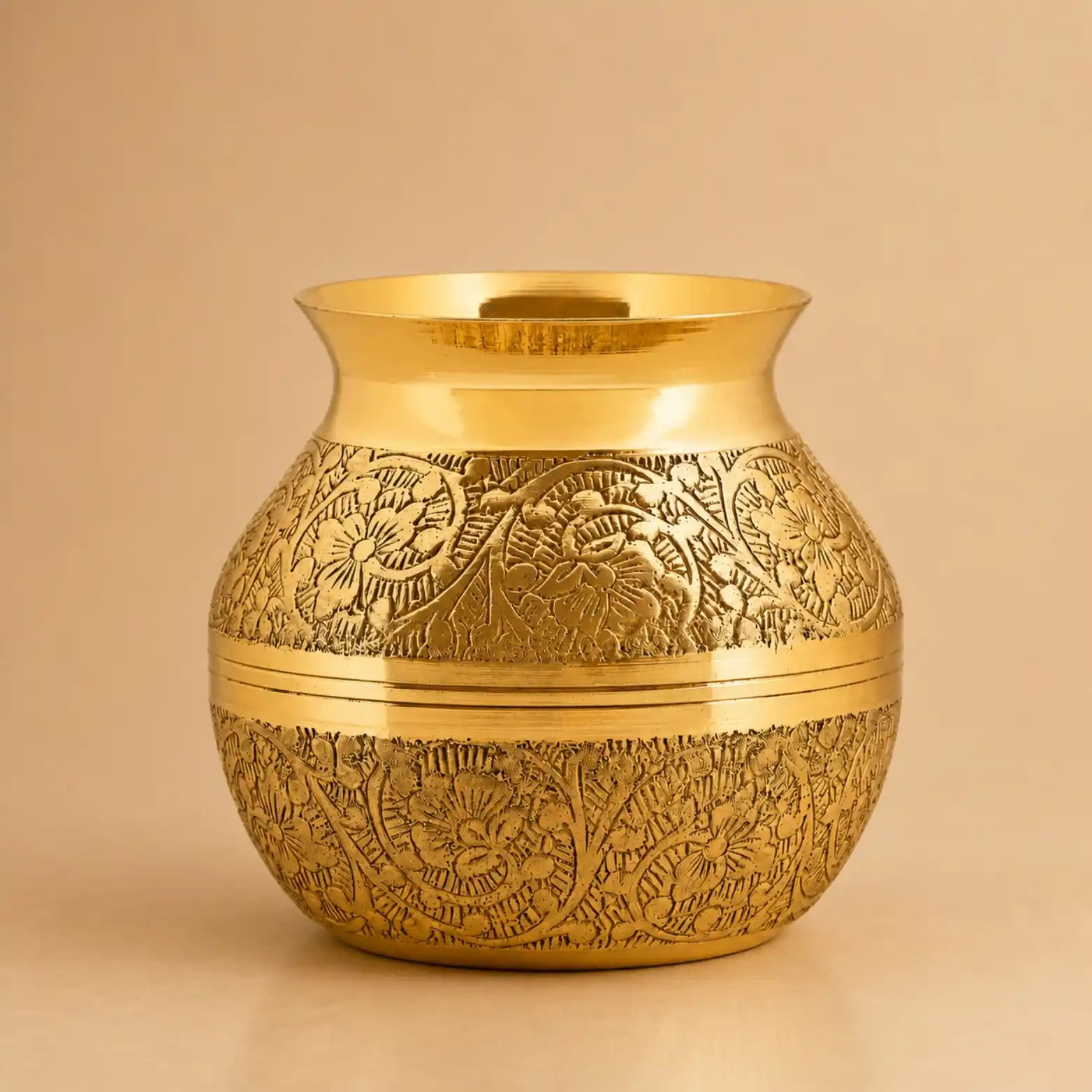 A small round gold-toned decorative pot with embossed floral and leaf patterns, shown on a plain beige background.