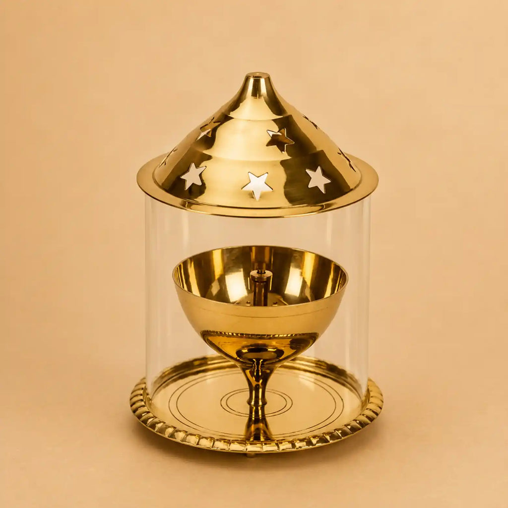 A polished gold-toned metal dreidel set inside a clear cylindrical glass or acrylic display case with a matching lid featuring star cutouts, photographed on a warm beige background.