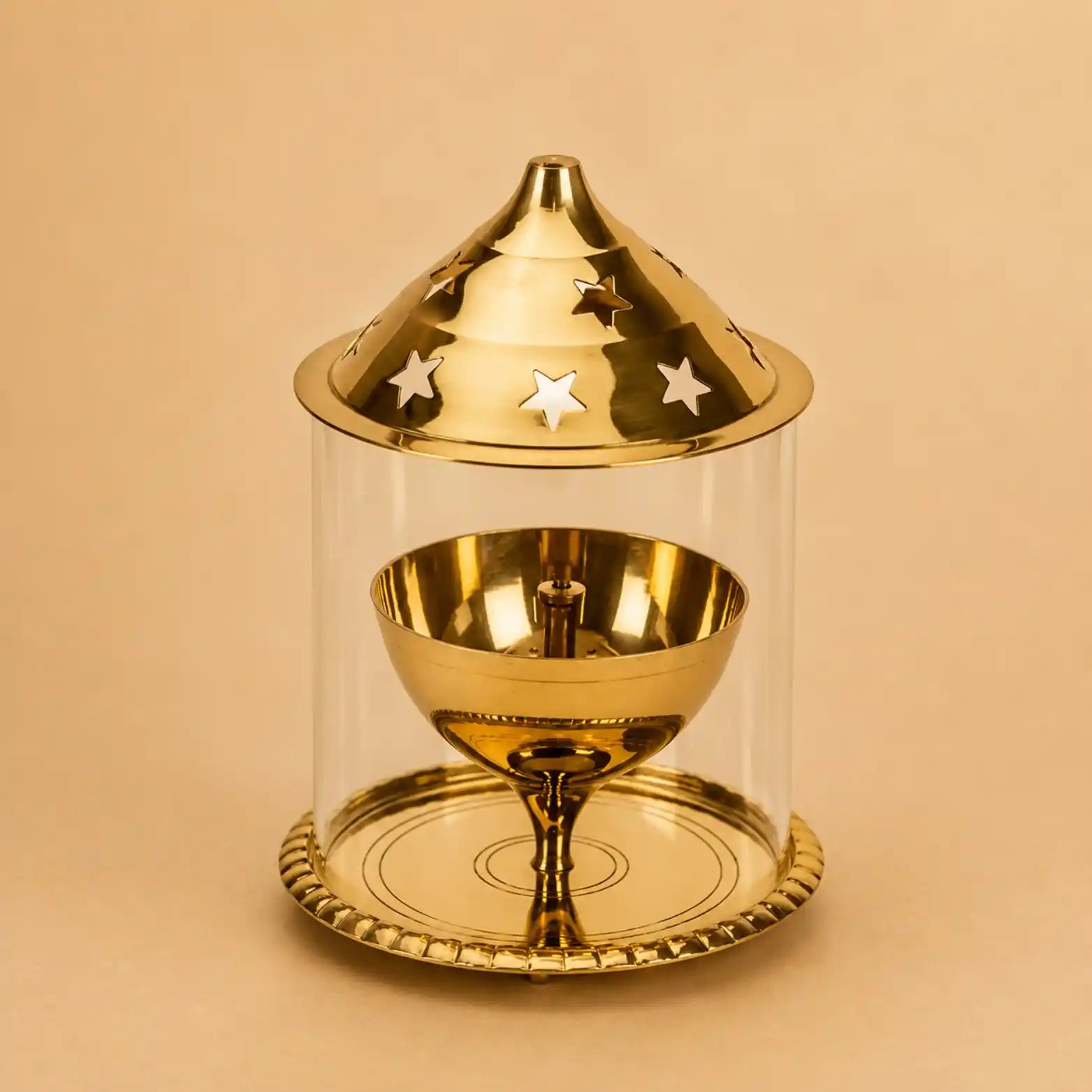 A polished gold-toned metal dreidel set inside a clear cylindrical glass or acrylic display case with a matching lid featuring star cutouts, photographed on a warm beige background.