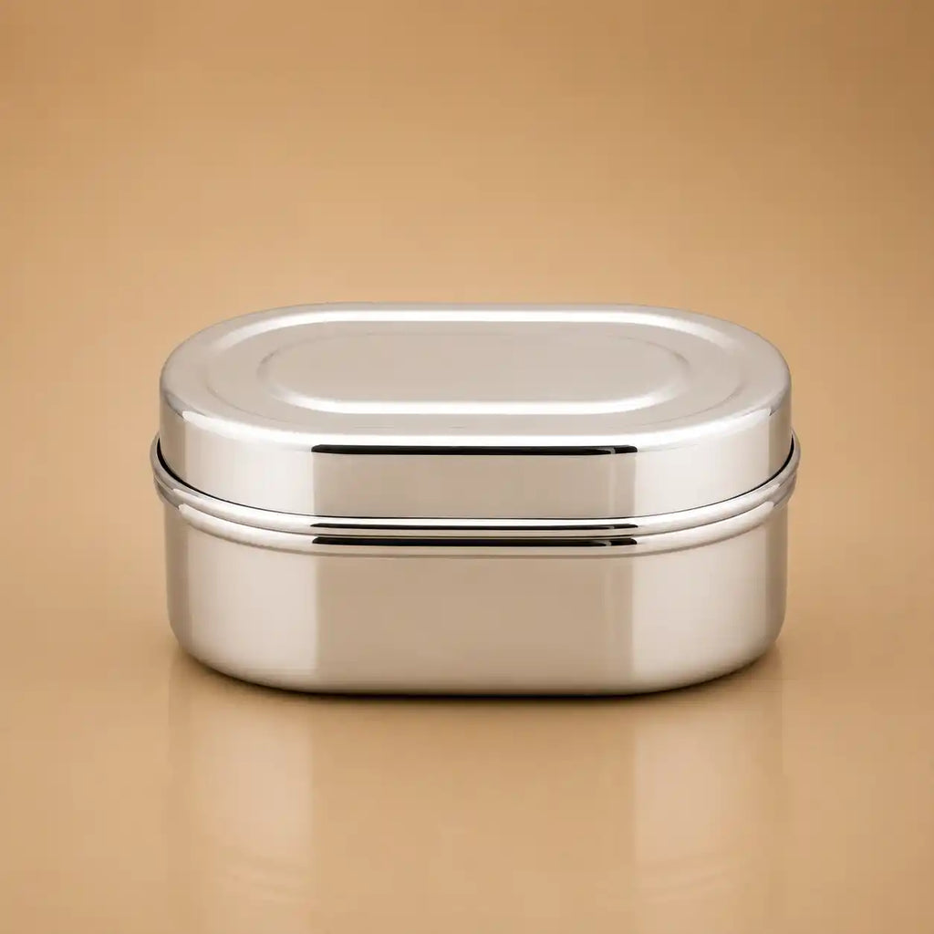 A stainless steel oval lunch box with a secure lid, shown on a warm beige background.