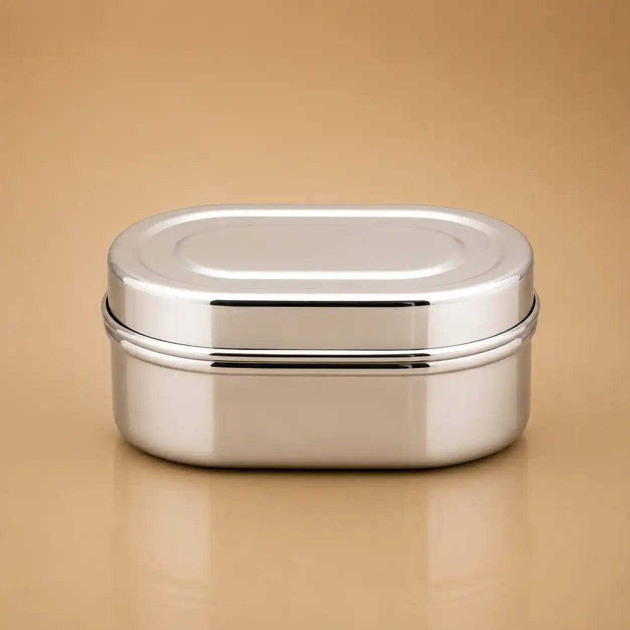 A stainless steel oval lunch box with a secure lid, shown on a warm beige background.