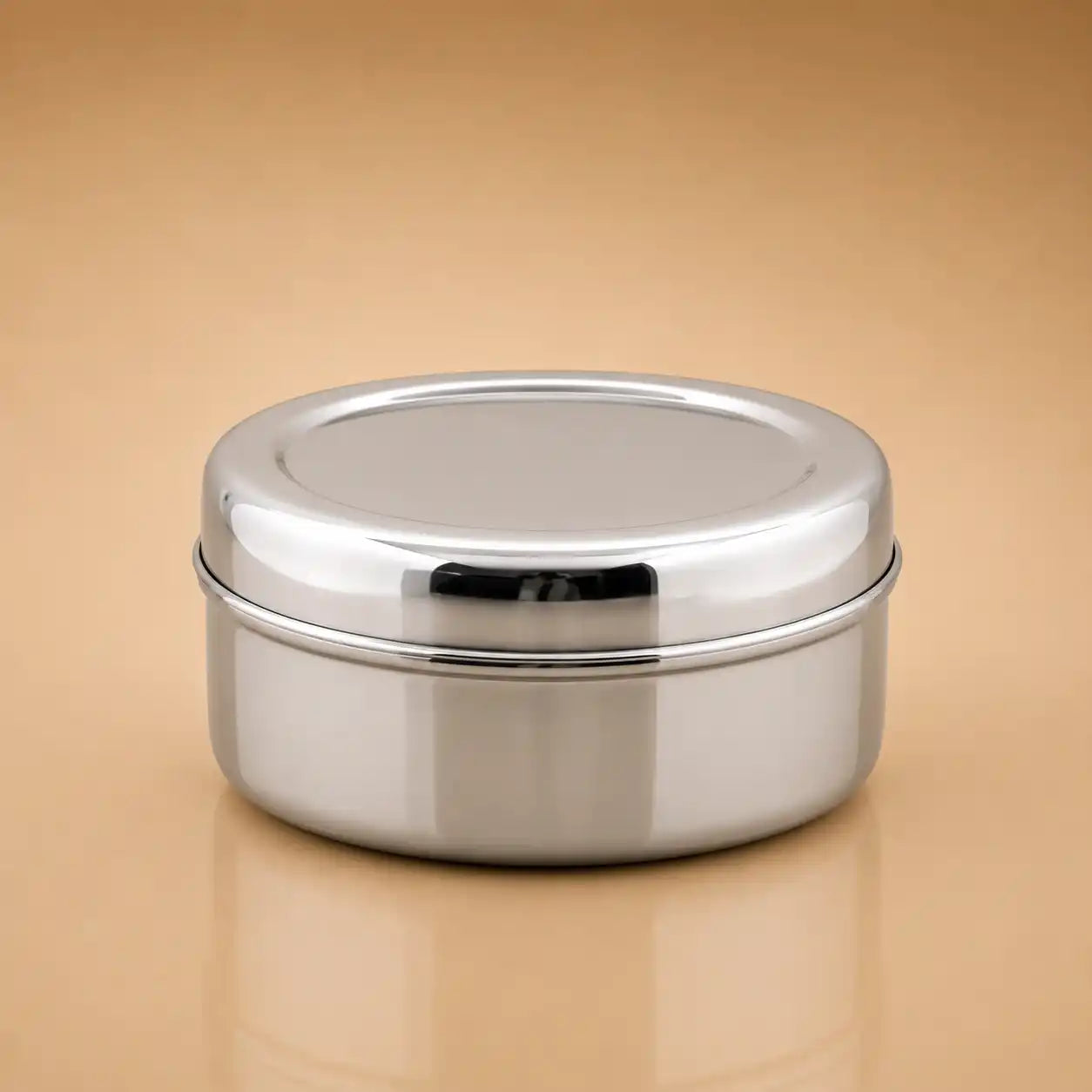 A round stainless steel lidded container with a polished metallic finish, shown on a warm beige gradient background.