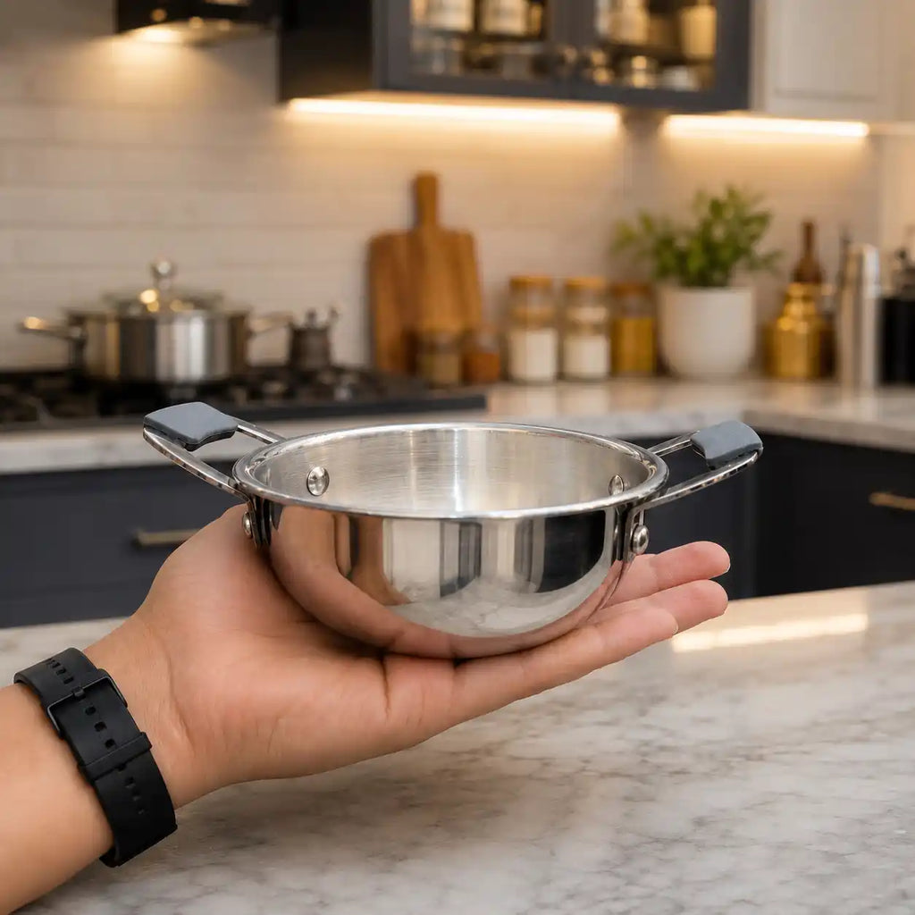 A hand holds a small stainless steel pot with black handles in a modern kitchen setting.