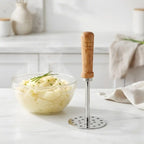 Mashed potato masher with a bowl of mashed potatoes on a kitchen counter.