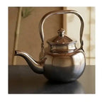 Silver teapot on a reflective surface with a blurred background