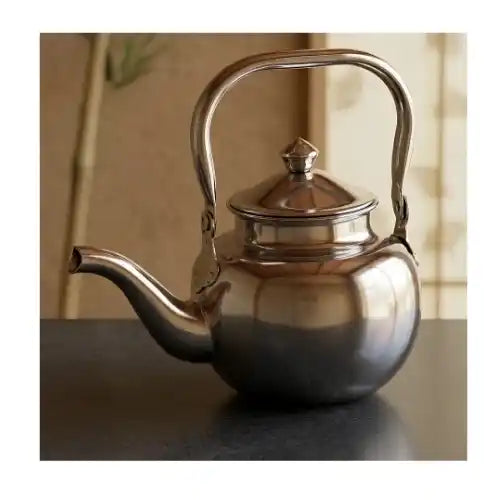 Silver teapot on a reflective surface with a blurred background