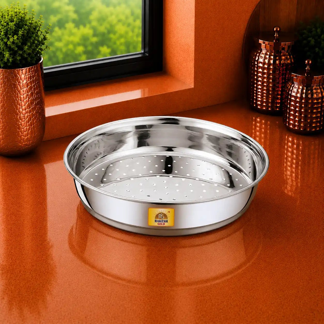 Stainless steel chalni (strainer) on a warm modern kitchen countertop with a window view, decorative plant, and copper storage jars.