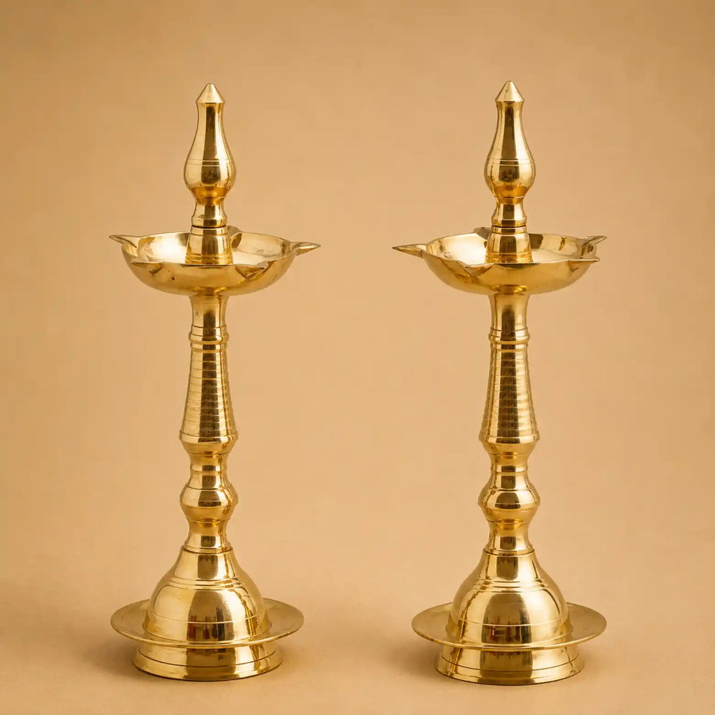 Two traditional brass oil lamps with ornate fluted stems and pointed finials, shown side by side against a warm beige background.