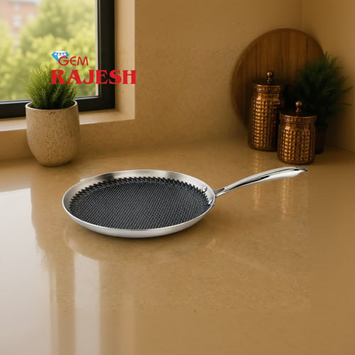 A stainless steel frying pan with a textured black non-stick coating and a long polished handle, placed on a beige countertop in a kitchen setting. A 'GEM RAJESH' logo is visible in the top left corner.