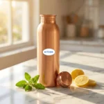Pure copper water bottle on marble countertop with tulsi leaves and lemon slices in warm kitchen lighting