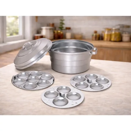 Aluminium idli maker steamer with lid and three idli plates placed on a kitchen countertop, traditional Indian idli cooking vessel set.