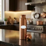 Pure copper water bottle on marble countertop with tulsi leaves and lemon slices in warm kitchen lighting