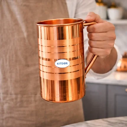Polished copper water jug with lid and handle placed on marble kitchen countertop