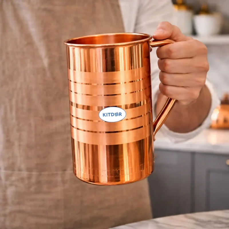 Polished copper water jug with lid and handle placed on marble kitchen countertop
