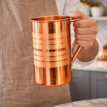 Polished copper water jug with lid and handle placed on marble kitchen countertop