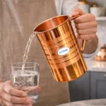 Polished copper water jug with lid and handle placed on marble kitchen countertop