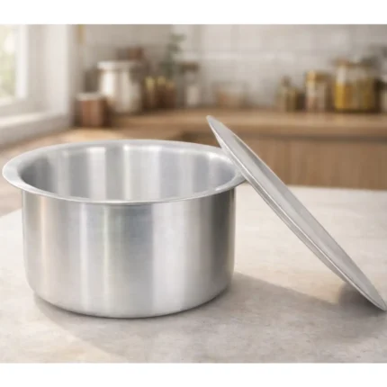 Stainless steel tope cooking vessel with lid placed on wooden kitchen counter, polished finish Indian kitchen cookware